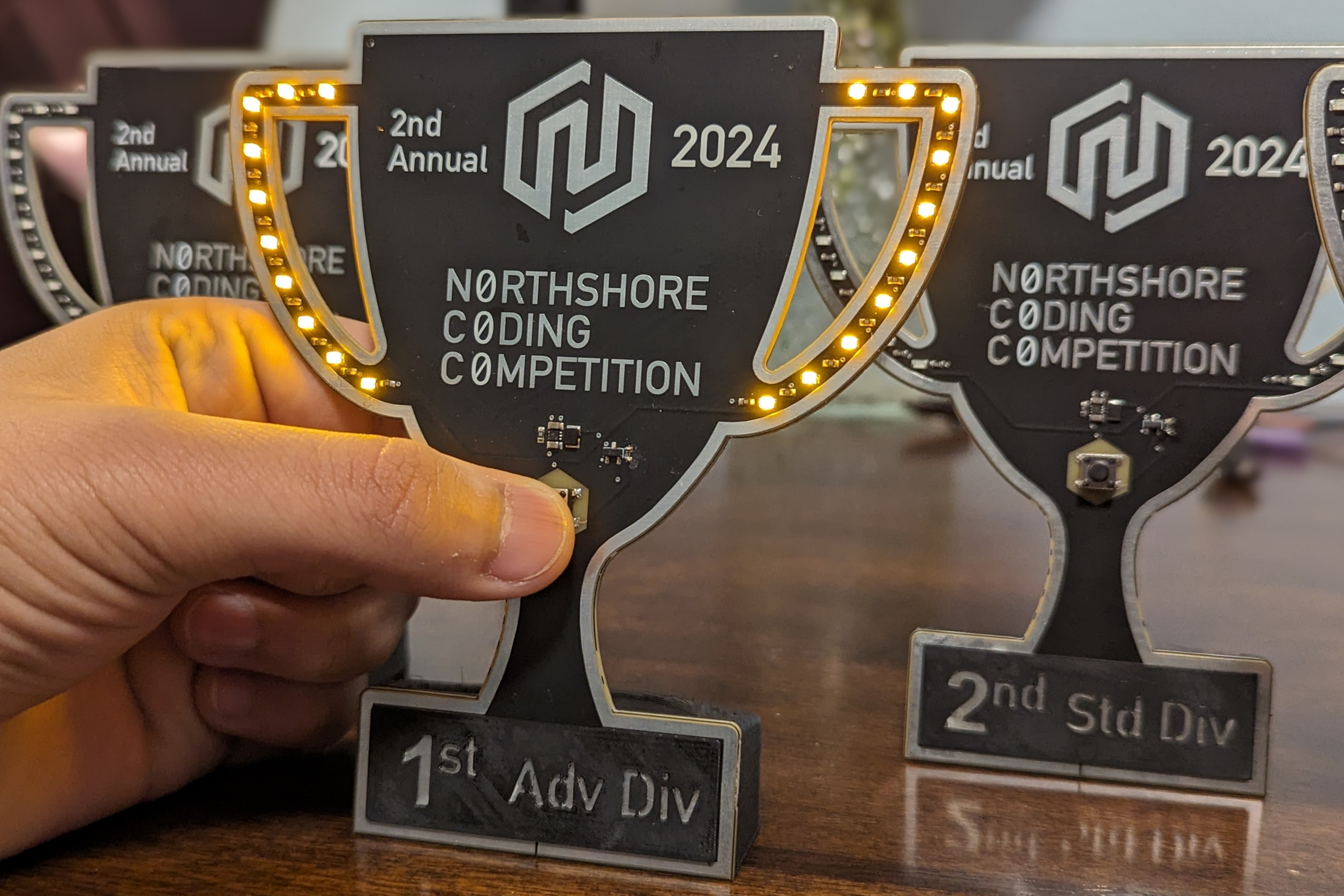 A trophy-shaped PCB with battery-powered lighting. Decorated with vector-defined copper regions, solder mask exclusions, and silkscreen.